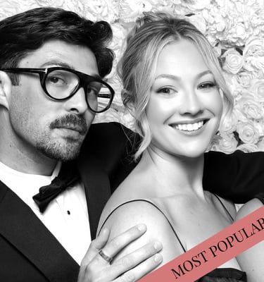 Elegant couple posing for a black and white wedding photo booth portrait with a flower wall backdrop.