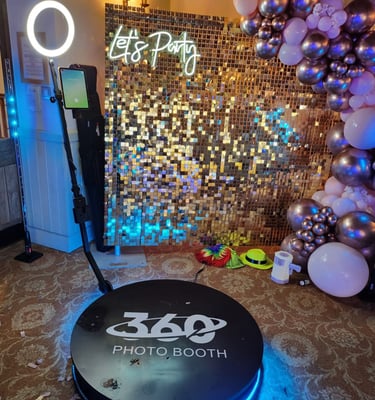 A 360 photo booth with ring light and gold shimmer wall backdrop for event party rentals.