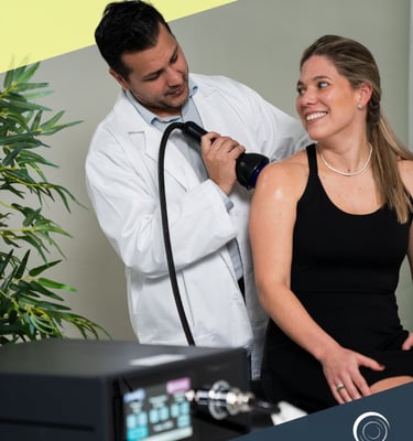 A doctor performing shockwave therapy on a woman's shoulder using an Omniwave medical device.
