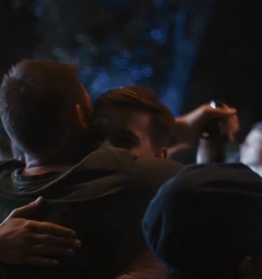 Two friends hugging and enjoying a night out at a crowded music festival or outdoor concert.