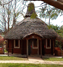 Traditional round African hut with a thatched roof and brown walls in a lush tropical garden.