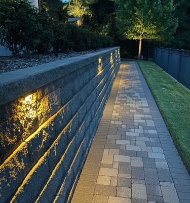 Illuminated stone paver walkway with landscape lighting embedded in a retaining wall.
