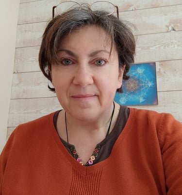 A middle-aged woman with short brown hair wearing an orange sweater and glasses indoors.