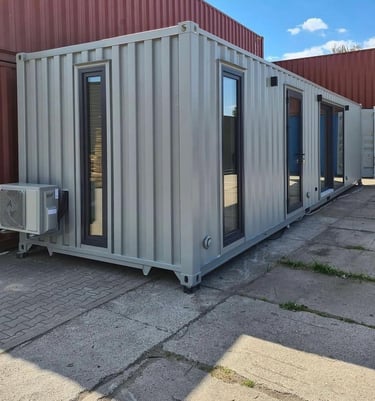 A gray shipping container home conversion with glass doors, windows, and an outdoor air conditioning unit.