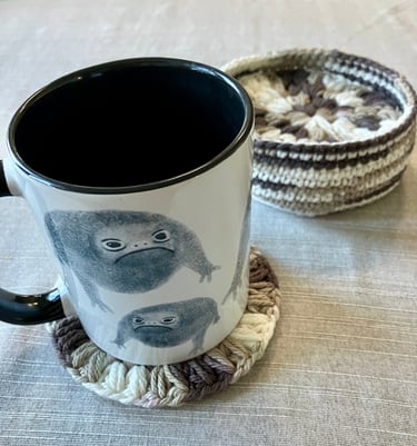 A mug on top of a crocheted drink coaster with more coasters inside a crocheted holder.