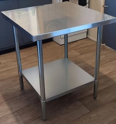 Commercial stainless steel work table available for table hire with solid under shelf and adjustable legs.
