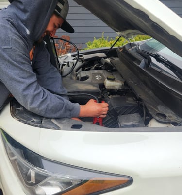 Auto Technician Dontez using a portable power unit to perform a battery jump start service for a customers vehicle in Central