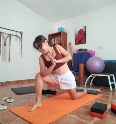 Mujer practicando postura de yoga de zancada baja sobre esterilla naranja en un estudio de Oaxaca