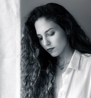Black and white portrait of a woman with long curly hair, looking down under soft studio lighting.