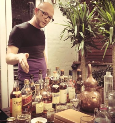 a man in a black shirt is standing in front of a table with bottles of whisky