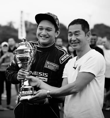 Keiichi Tsuchiya handing a trophy to a man in front of a crowd