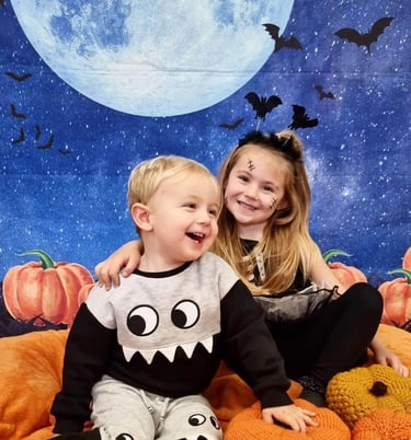 2 children, brother and sister dressed up for halloween sat surrounded by pumpkins