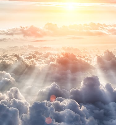 Photo of a group of clouds seen from above, with a heavenly light shining from afar
