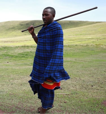 A Maasai Warrior in a blue and black outfit holding a stick in his hand