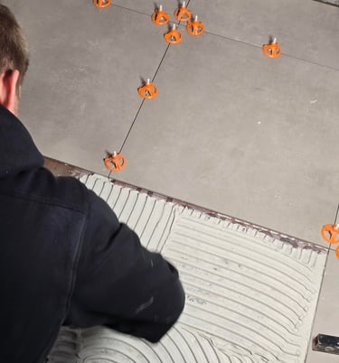 Professional contractor installing large format floor tiles with orange leveling spacers and thinset mortar.