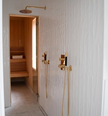 Modern luxury walk-in shower with gold fixtures and white subway tile next to a wood-paneled home sauna.