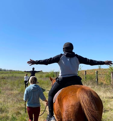un jeune homme monté à cheval écartant grand les bras lors d'une séance d'équithérapie