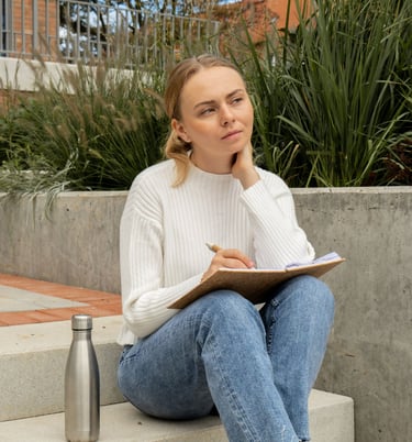 a woman sitting on a concrete step reflecting on herself writing her accomplishments