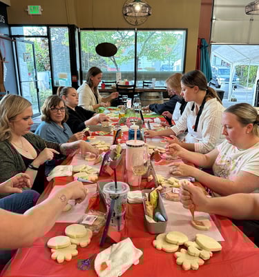 a group of people sitting at a table decorating cookies