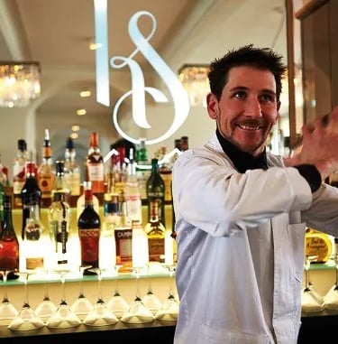 a man in a white shirt is holding a shaking a cocktail shaker