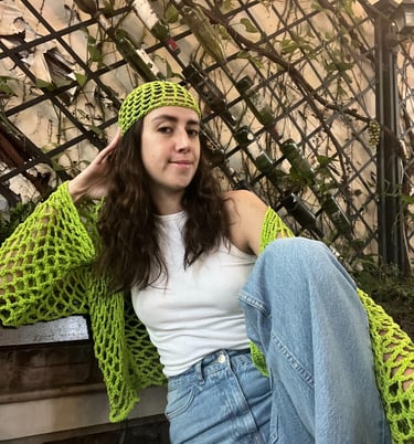 A woman posing on a bench, wearing her stylish green croquet long sleeved top and beanie. 