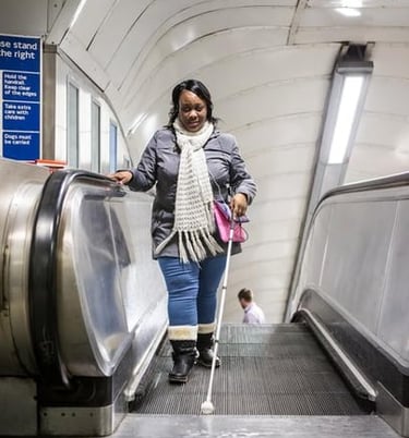 Woman using a cane while getting off an escalator, demonstrating mobility for the visually impaired.