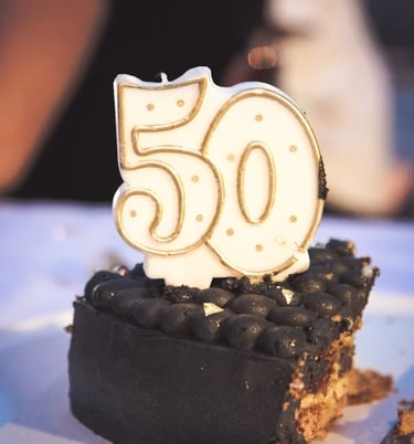 A 50th birthday candle with gold trim on a slice of gourmet dark chocolate cake.