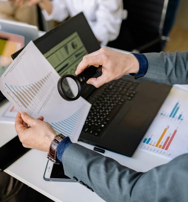 Un hombre revisa un documento en una computadora portátil con una lupa.