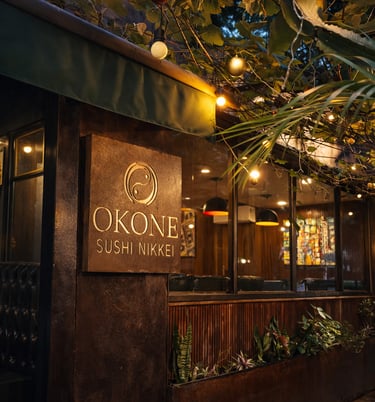 Close da placa de madeira com o logotipo dourado do Okone Sushi Nikkei na fachada do restaurante
