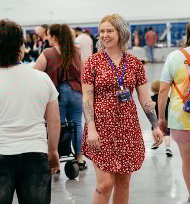 A woman in a red dress with a volunteer badge smiles at event goers