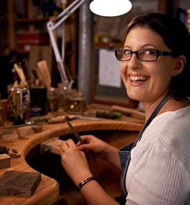 Joyera artesana sonriente trabajando con herramientas manuales en un banco elaborando joyeria