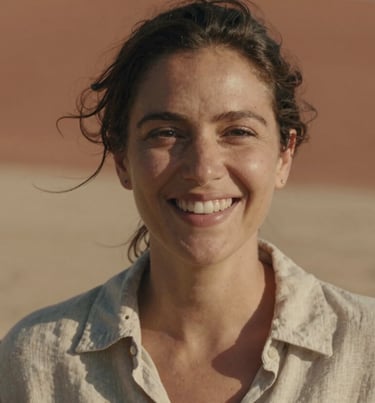 Close-up portrait of a smiling woman in a linen shirt, natural cinematic lighting, warm sand and terracotta background, authentic expression.