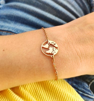 Dainty gold chain bracelet featuring a circular world map globe charm on a person's wrist.