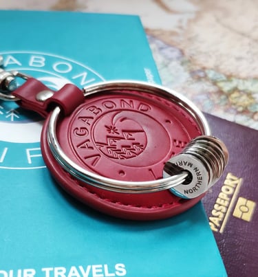 Red leather Vagabond Life travel keychain with silver rings on a passport and world map.