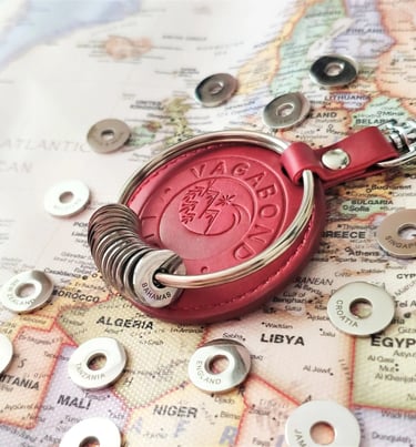 Red leather Vagabond travel keychain with engraved country rings on a world map.
