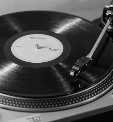A sleek, black-and-white professional photograph of a vinyl record spinning on a modern turntable, emphasizing high-fashion minimalist aesthetics, North American / US music culture.