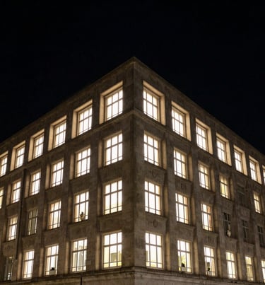 Night view of a illuminated architectural facade, carbon black sky, warm light spilling from windows, sharp geometric forms.