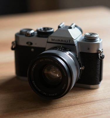 Close-up of a vintage camera on a wooden table. Warm moody lighting with soft Charcoal (#333333) shadows and Soft Sand (#F8F0E3) highlights.