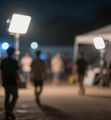 A blurred, atmospheric shot of a North American film set at night. The soft focus creates beautiful bokeh of blue and off-white lights, suggesting a high-budget production environment.