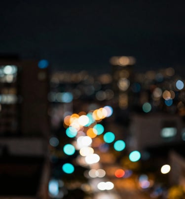 Artistic bokeh shot of city lights in Bogotá, showcasing deep blacks and vibrant neon cyan circles. Cinematic and urban.