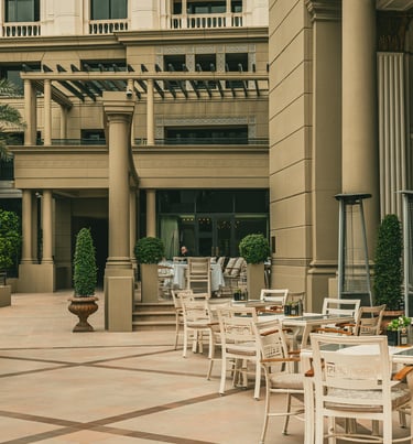 Elegant outdoor patio seating at a luxury hotel with white chairs and classical architecture.