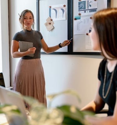 A young professional woman presents design concepts on a whiteboard during a creative office meeting.
