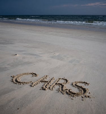 Cinematic vertical shot of the empty beach at twilight, the remnants of sand art visible, soft sand off-white meeting the dark sea.