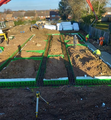 Construction site workers using a red concrete pump to pour foundations with steel reinforcement mesh.