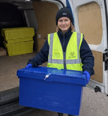 A smiling TTB Circular employee holds a security-sealed crate next to an open van.