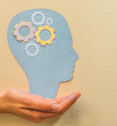 Nell'immagine si vede una mano che sostiene la sagoma di una testa, con degli ingranaggi lavoranti