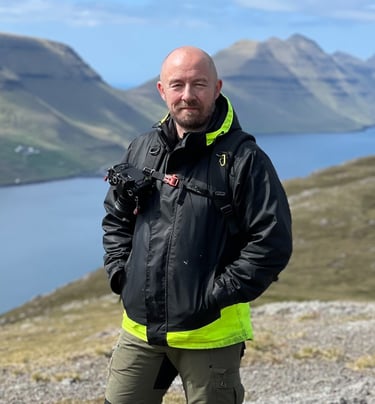 Bogi Olsen, your local Faroe Islands photography guide, standing outdoors with camera gear and scenic fjords behind him