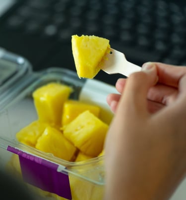 atidarytas pjaustytų ananasų indelis ir vienas gabaliukas yra pasmeigtas ant šakutės