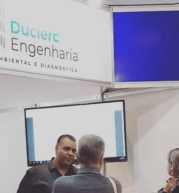 Representante da Duclerc Engenharia atendendo cliente durante feira técnica, apresentando serviços d