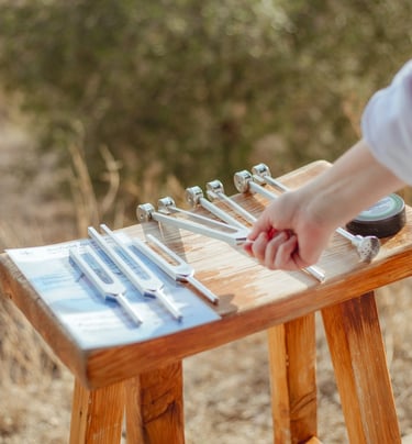Close up of Sheila Doerlfer's hand choosing one of 6 tuning forks on a wood stool with Spanish country side 